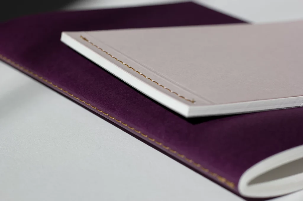 Deux carnets faits main à l'atelier Forme contre forme avec une reliure Singer : un avec couverture violette cousu à cheval, l'autre en paysage avec couverture rose pâle cousu à plat.