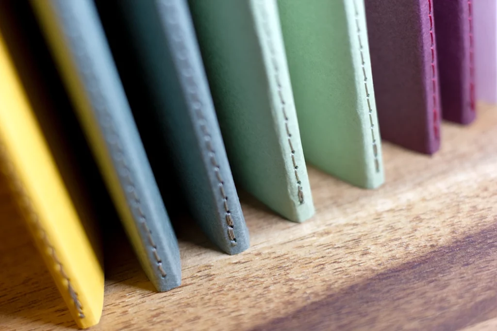 Zoom sur le bas des carnets faits main à l'atelier Forme contre forme avec une reliure Singer et des couvertures colorées en vues de dos. Zoom sur le bas des carnets faits main à l'atelier Forme contre forme avec une reliure Singer et des couvertures colorées en vues de dos.
