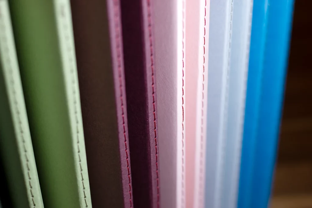 Zoom sur les carnets faits main à l'atelier Forme contre forme avec une reliure Singer et des couvertures colorées en vues de dos. Zoom sur les carnets faits main à l'atelier Forme contre forme avec une reliure Singer et des couvertures colorées en vues de dos.
