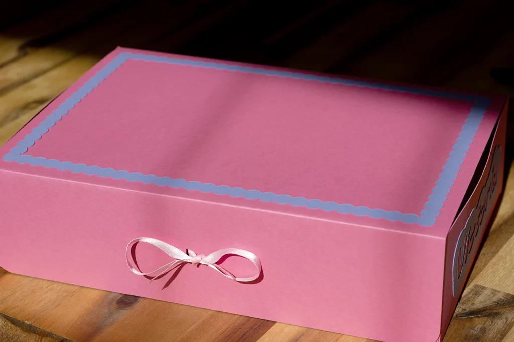 Coffret fermé, rose avec cadre violet lavande, décoré et fermé par un ruban rose — jeu "Au royaume des licornes".