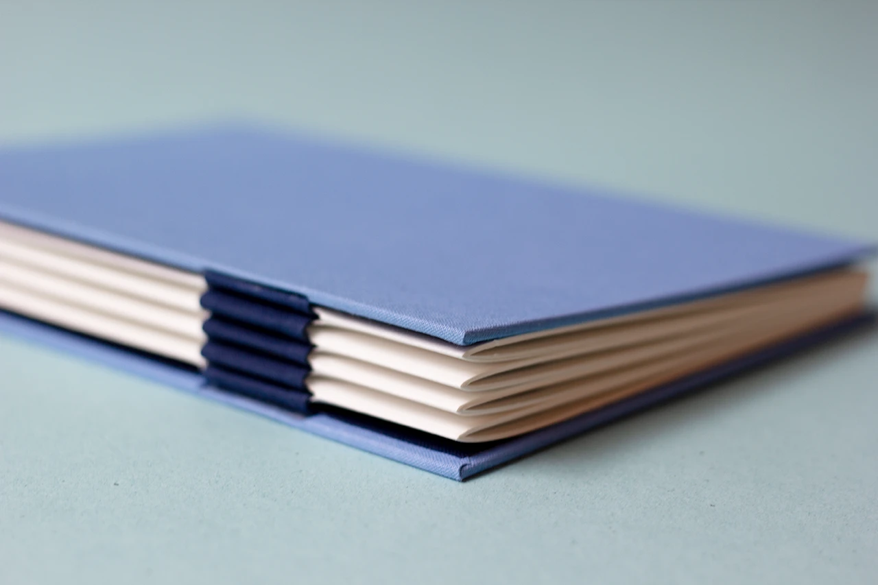 Zoom sur le bas du dos du carnet, présentant une reliure australienne à charnière piano inversée, style plat.