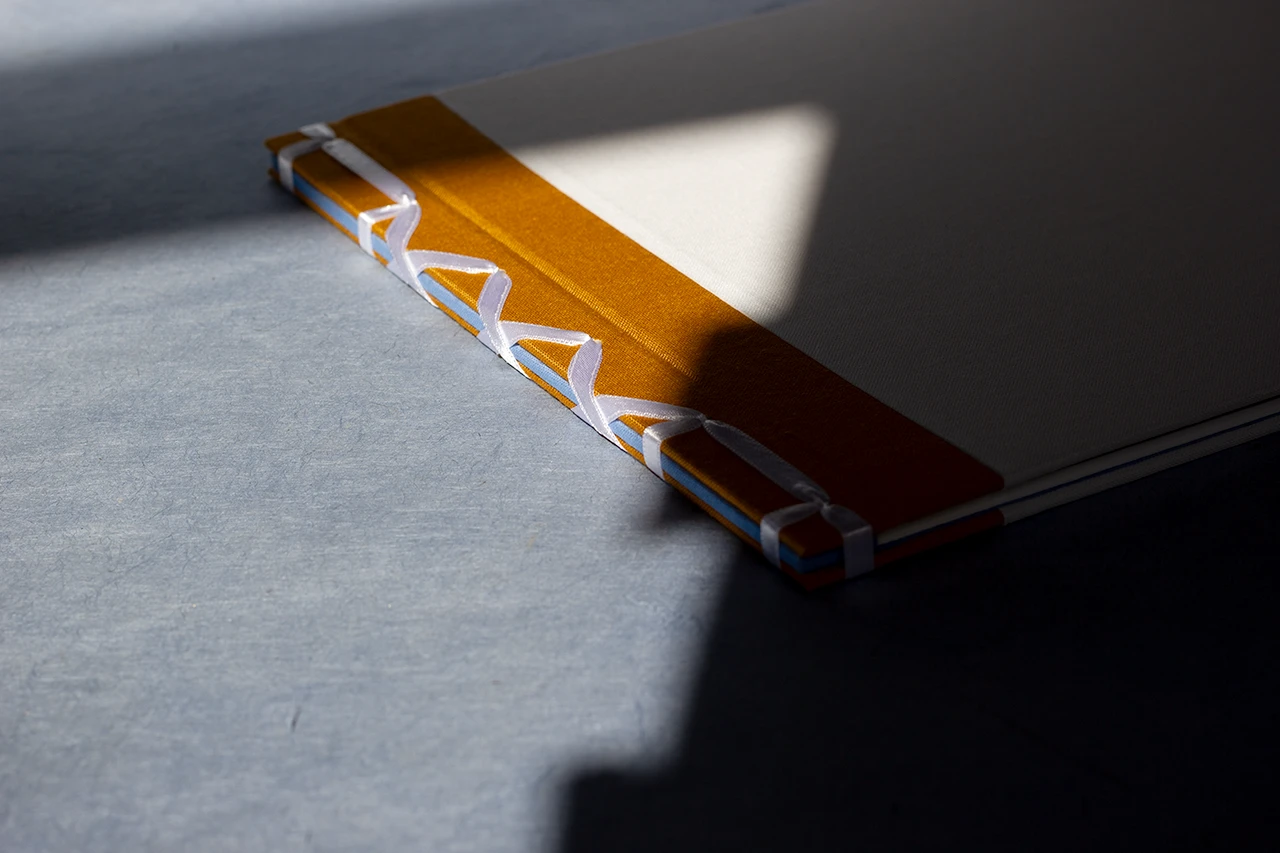 Carnet en reliure japonaise, ruban satiné blanc, couverture en toile du Marais blanche et pièce jaune moutarde, dos en toile bleue apparent — Atelier Forme contre forme, Bordeaux.