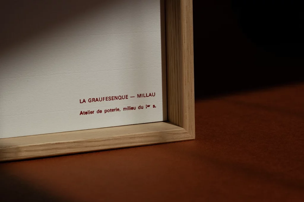 Zoom sur le titrage du cartel « La Graufesenque — Millau » en dorure à chaud rouge brique sur papier vergé — Atelier Forme contre forme, Bordeaux.